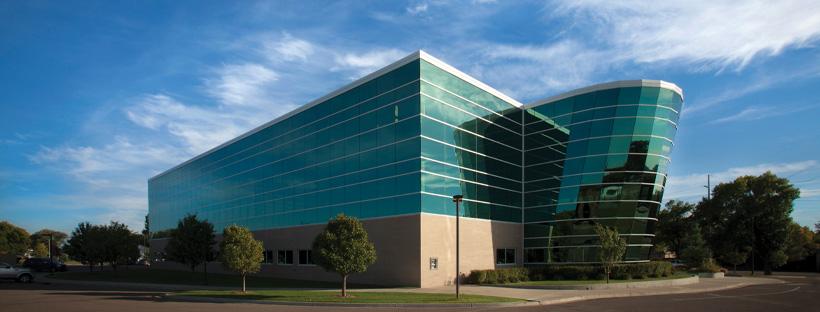 A photo of the Bank of North Dakota, a multi-story, window-covered building against a blue sky with cloud wisps. 