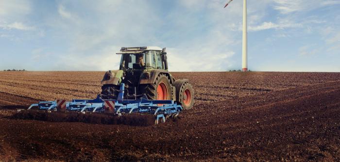 Image: tractor on a field with a wind turbine. Topic: Regenerative Agriculture.