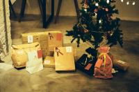 gifts wrapped in brown paper bags and cloth bags under a small christmas tree