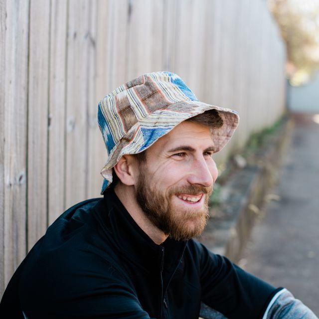 A white man wearing a bucket hat and smiling. Sustainable summer.