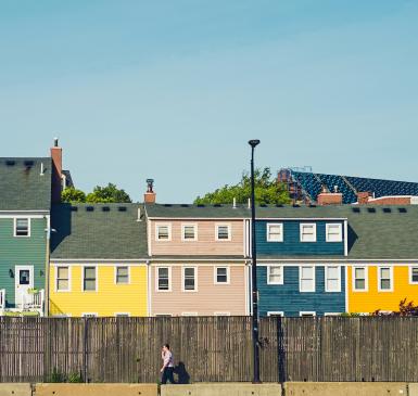 Image: person walking by row of homes. Topic: Green Home.