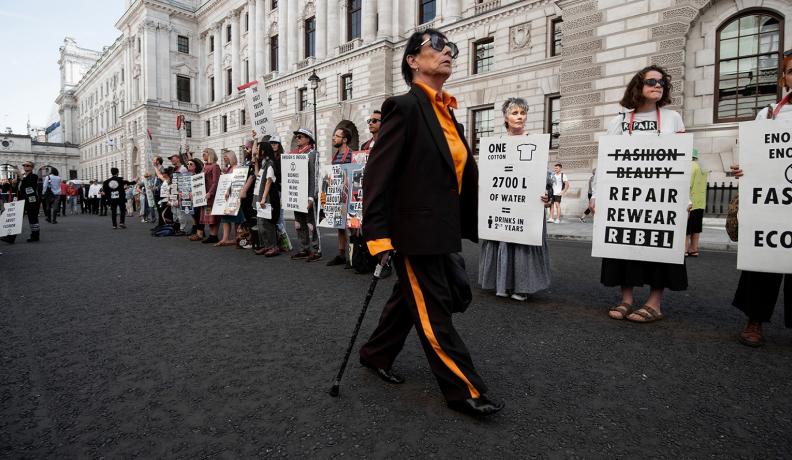 woman in black and yellow outfit walks in front of line of climate protestors from Extinction Rebellion