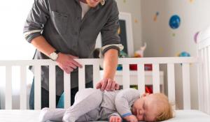 Image: father smiling over baby in crib. Organic baby products.