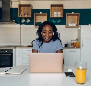 A young Black woman looks for financial information on her laptop in her kitchen
