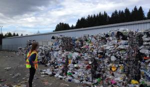 Image: person standing in front of large piles of recyclables. Topic: Does Recycling Help the Climate?