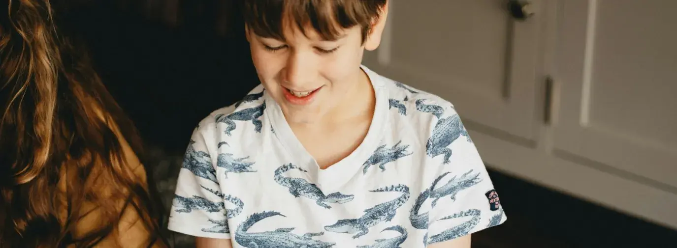 a boy of about ten years old reads a clue off a strip of paper. He is smiling and wearing a cotton t-shirt with alligators on it. His sister sits next to him, reading off the paper.