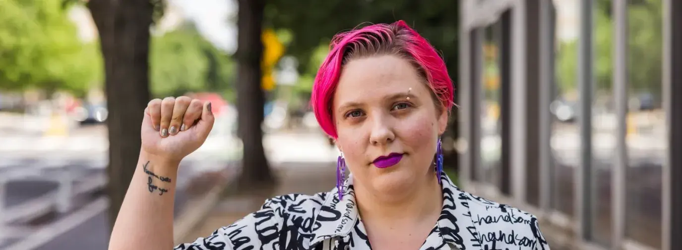 Anya stands facing the camera with a soft smile, holding up one hand in a fist.