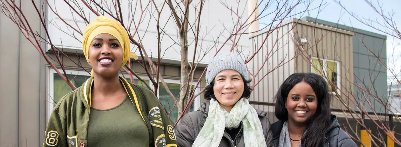 Image: three people stand outside a new housing development. Topic: Turning Crisis into Creation with Green Affordable Housing