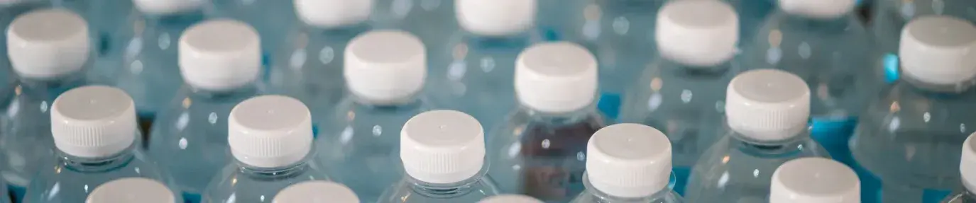 macro shot of rows of clear plastic water bottles with white caps; plastics greenwashing is bad
