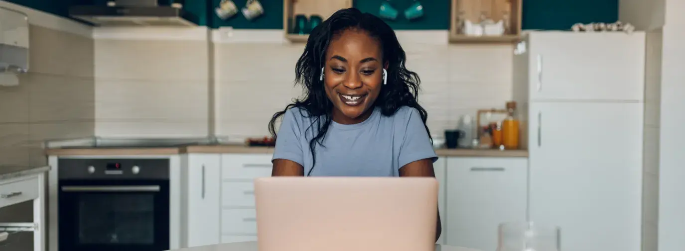 A young Black woman looks for financial information on her laptop in her kitchen