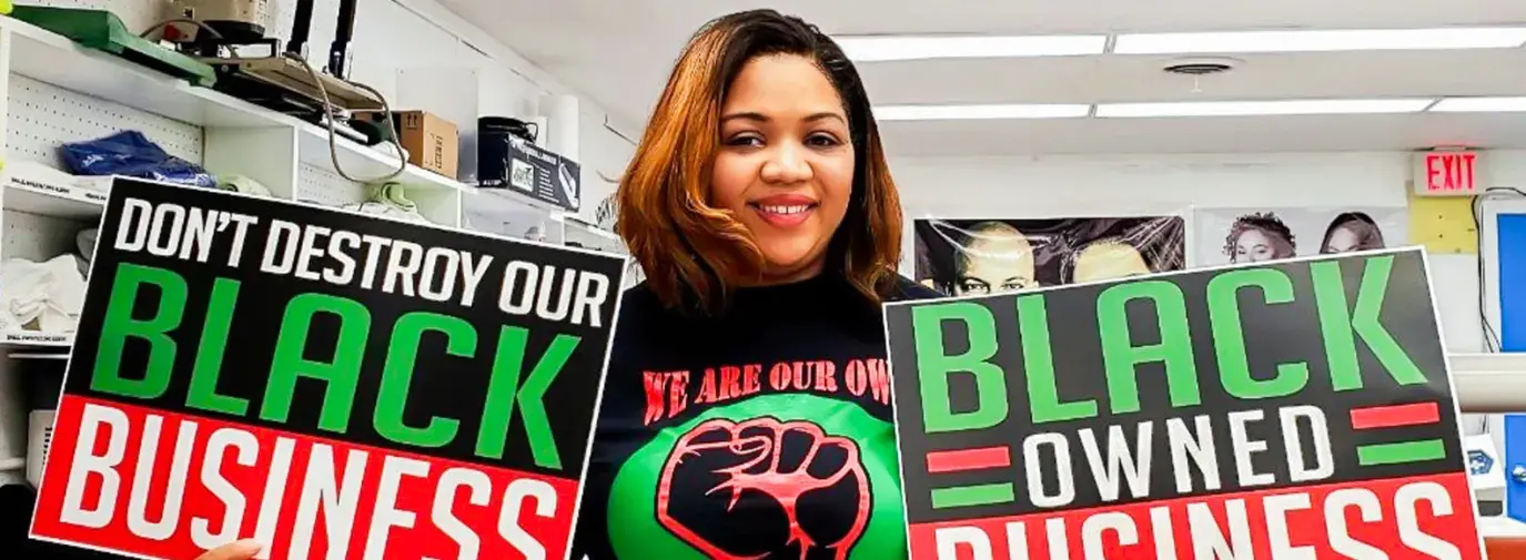 Keeanna Barber of WDB Marketing holds signs that say "Don't destroy our Black Business" and "Black Owned Business" that she printed at her shop.